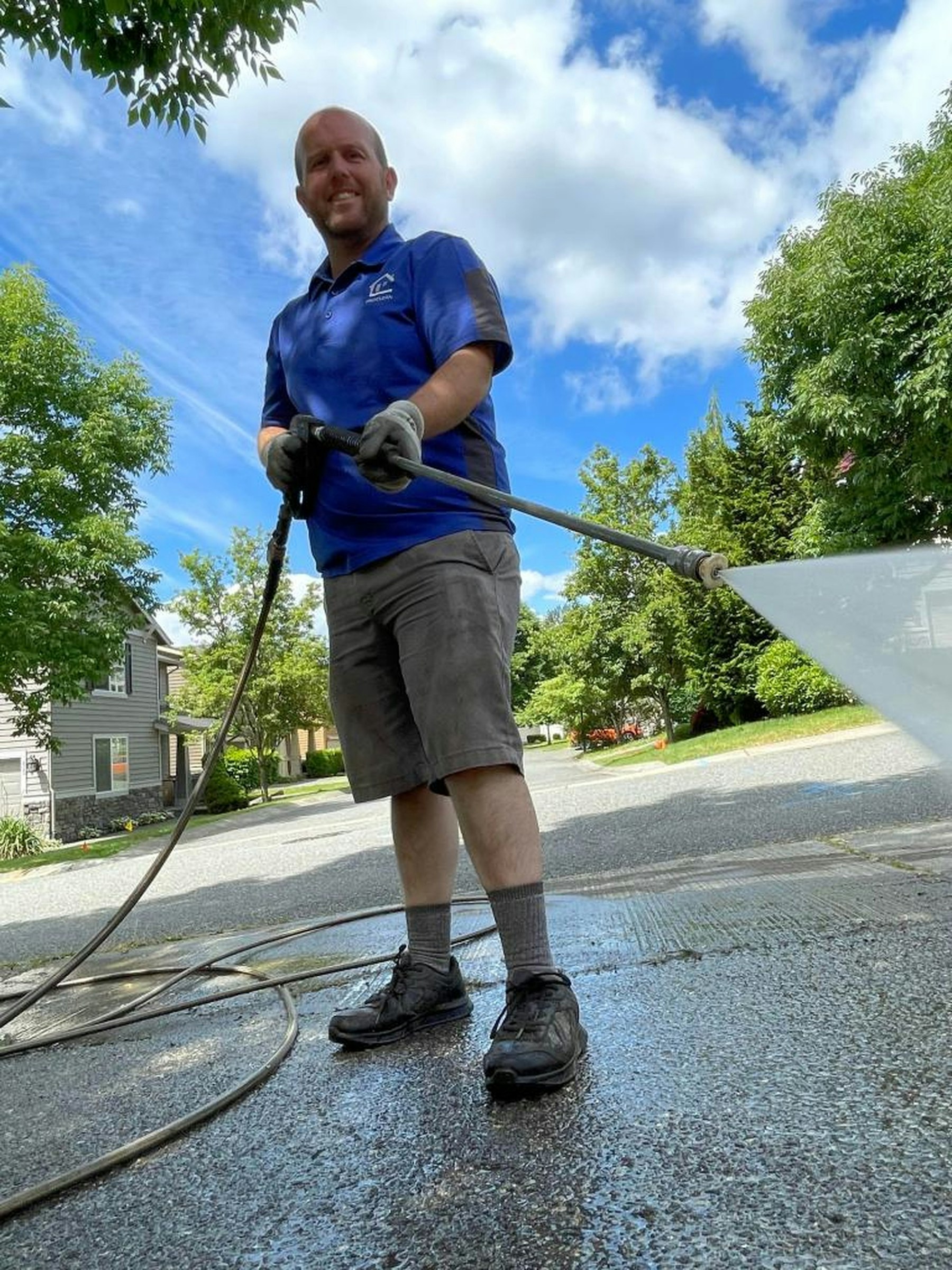 A cleaner in a blue shirt pressure washing a driveway
